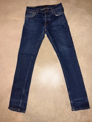 🔥 NUDIE JEANS CO – PREMIUM DENIM | SNABB SÄLJ 🔥 - Riktigt feta Nudie Jeans Co i mörk indigo med clean look. Klassisk modell som alltid funkar – enkel att styla, sitter bra och åldras snyggt. Nudie-denim är gjord för att användas, inte ligga i garderoben.  Jeansen är använda och har ett hål (se bild) – ger en rå, worn-in vibe. Perfekt om du gillar vintage / street / repair-core eller vill laga själv. Priset är satt därefter → 299 kr = STEAL.  💥 Premium denim 💥 Tidlös passform 💥 Äkta Nudie – inga kopior 💥 Pris för snabb affär  Först till kvarn, i