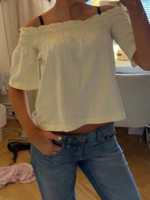 Ljus gul offshoulder topp med kort ärm - Säljer en söt ljus gul offshoulder topp med korta ärmar och smockad kant upptill. Toppen har en luftig passform och är perfekt för varma dagar. Enkel och stilren design som passar till mycket.
