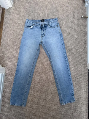 Ljusblå raka jeans - Säljer ett par ljusblå jeans med rak passform och klassisk femficksdesign. Jeansen har normal midja och är tillverkade i denim med en snygg tvättad look. Perfekta för en avslappnad stil och passar till det mesta i garderoben.