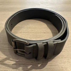 Grått mocka bälte med silverfärgat spänne - Snyggt grått mocka bälte med ett stilrent silverfärgat spänne. Tillverkat i ett robust material med flera justerbara hål för perfekt passform. Perfekt för att komplettera din outfit. 9/10 skick användt 4-5 gånger. 100cm långt 3cm bredt