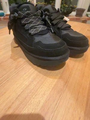 Ugg lowmels - Snygga svarta sneakers från UGG med chunky sula och breda, mönstrade skosnören. Skorna har en mix av mocka och textilmaterial som ger en cool och modern look. Perfekta för dig som gillar streetstyle och vill ha något unikt på fötterna. Nästan helt nya! Köpte för 3000 mitt pris 1499 köpte i november detta år! Kom priv för fler bilder! Pris kan diskuteras!