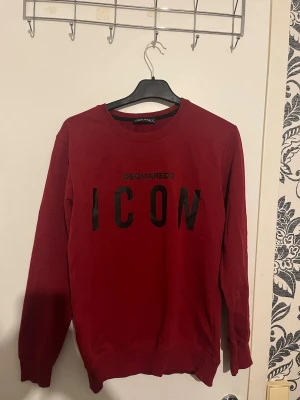 Röd sweatshirt från Dsquared2 ICON - Cool röd sweatshirt från Dsquared2 med svart 'ICON'-tryck på bröstet. Tröjan har rund halsringning, långa ärmar och ribbade muddar. Perfekt för en trendig och avslappnad stil. Storlek xs 