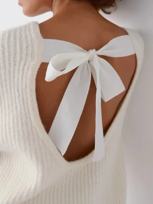 Vit stickad tröja med rosett i ryggen - Superfin vit stickad tröja med öppen rygg och stor vit rosett som detalj. Tröjan har breda ärmar och är ribbstickad för en mysig känsla. Perfekt för dig som vill ha något unikt och trendigt i garderoben.