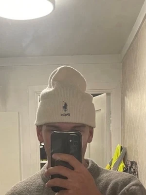 Vit ribbstickad mössa från Polo Ralph Lauren - Snygg creme vit ribbstickad mössa från Polo Ralph Lauren med klassisk broderad logga framtill. Mössan har uppvikt kant