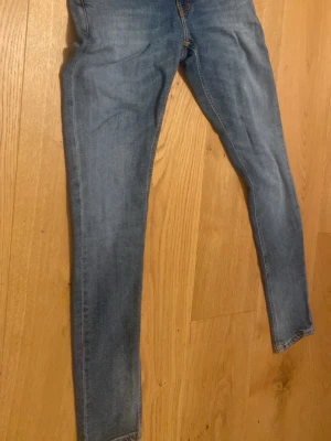 Blå skinny jeans från Nudie Jeans size 27:32 - Säljer ett par blå skinny jeans från Nudie Jeans med klassiska orange sömmar och snygga detaljer på bakfickorna. Jeansen har en smal passform och är tillverkade i mjukt denimtyg. Perfekta för en avslappnad och trendig look.  Kan också tänka mig byta jeans 