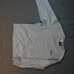 Grå sweatshirt från Frank Dandy - Snygg grå sweatshirt från Frank Dandy med rund halsringning och svart logotyptryck på bröstet. Tröjan har en klassisk passform och är tillverkad i mjukt material, perfekt för en avslappnad stil.