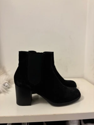 Svarta Chelsea boots med klack - Snygga svarta Chelsea boots i mockaimitation med bred resår på sidorna och stabil blockklack. Klassisk siluett med rundad tå och enkel design som passar till många olika stilar. Perfekta för dig som vill ha både stil och komfort.