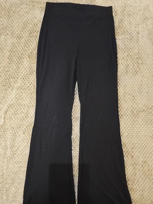 Svarta kostymbyxor från H&M Divided - Säljer ett par svarta kostymbyxor från H&M Divided med diskreta ränder. Byxorna har utsvängda ben och är tillverkade i ett stretchigt material av 91% polyester och 9% elastan. Perfekta för en stilren och trendig look.