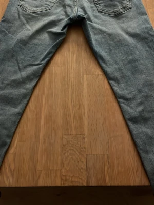 Gråblå raka jeans med bakfickor - Snygga gråblå jeans med klassisk rak passform och två bakfickor. Jeansen har en enkel design utan synliga loggor och är tillverkade i denim. Perfekta för en avslappnad och stilren look.