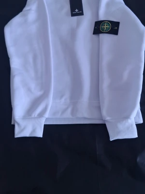 Stone Island helt vit sweatshirt | Storlek S | Ny med tag - Stone Island sweatshirt i helt vitt utförande, storlek S. Helt ny och aldrig använd – fortfarande med prislapp. Inga fläckar, märken eller defekter.  Detaljer: • Regular fit • Helt vit design • Avtagbar Stone Island-badge på ärmen • Mjukt polyestermaterial • Ribbstickade muddar och fåll • Passar perfekt för vardagsbruk, layering eller en clean streetwear-look  Material: • 100% polyester  Övrigt: • Förvarad i rökfritt hem • Snabb leverans
