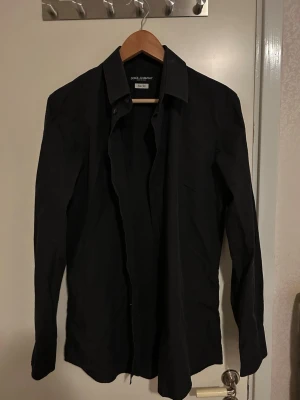 Svart skjorta Dolce & Gabbana Slim Fit - Säljer en svart långärmad skjorta från Dolce & Gabbana i slim fit-modell. Klassisk krage och knappar framtill. Tillverkad i Italien och har en stilren look som passar perfekt till många olika outfits.