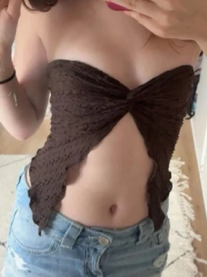 Brun bandeau tubtopp från Shein - Säljer en brun bandeau tubtopp från Shein i storlek XS. Toppen har en snygg omlott-design framtill med twistad detalj och spetsiga kanter. Materialet är strukturerad polyester med ett mönstrat tyg som ger en cool look. Perfekt för att styla med jeans eller kjol.