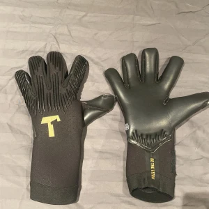 Titan Rebel 2.0 Black-Out målvaktshandskar storlek 9 - Säljer ett par svarta Titan Rebel 2.0 Black-Out målvaktshandskar med 4mm Gecko Grip för extra grepp. Får med handledsskydd, rengöringsspräj och målvakts lim för extra grepp. Påsen till handskarna hittar jag inte, använd kanske mellan 5-6 träningar och har inga slitningar. Ordinarie pris med allt 1300 kr