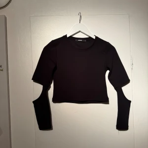Svart croppad topp från Bik Bok - Cool svart croppad topp från Bik Bok. Rund halsringning och lång ärm med cut-out som ger en edgy vibe. Perfekt för dig som vill sticka ut med din stil och gillar trendiga plagg. Storlek s