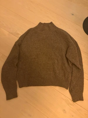 Brun stickad polotröja från H&M - Mysig brun stickad polotröja från H&M i storlek S. Tröjan har en hög krage och långa ärmar med ribbade muddar vid ärmslut och nederkant. Perfekt för kyliga dagar och enkel att matcha med jeans eller kjol.
