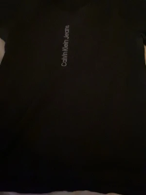 Svart t-shirt från Calvin Klein Jeans - Svart t-shirt från Calvin Klein Jeans med vertikalt tryck på bröstet. Klassisk passform och rund halsringning. Tillverkad i mjukt material som känns skönt mot huden. Perfekt för en clean och stilren look.