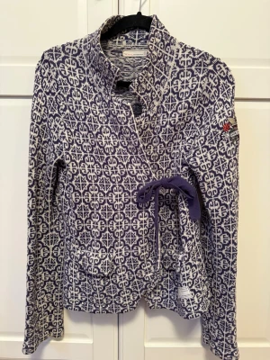 kofta från Odd Molly - Säljer en snygg blå och vit kofta från Odd Molly med unikt mönster och broderad detalj på ärmen. Koftan är stickad, har omlottmodell med knytband i midjan och långa ärmar. 