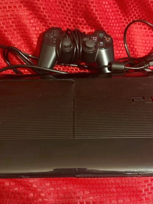 Sony PlayStation 3 Super Slim - Sony PlayStation 3 Super Slim med en originalkontroller och kablar. Konsolen har några synliga repor och mindre slitage på ytan, men är i gott skick. Diskfacket fungerar och alla knappar på kontroller ser hela ut. Perfekt för spel och multimedia.