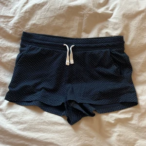 Mörkblå prickiga shorts från H&M - Säljer ett par mörkblå shorts från H&M med vita små prickar och snörning i midjan. De är gjorda i mjuk ekologisk bomull med lite stretch. Mycket bra skick utan fläckar eller slitage