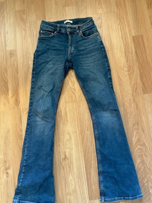 Blå bootcut jeans från Gina Tricot - Säljer ett par blå bootcut jeans från Gina Tricot, modell Perfect Jeans. Klassisk medelhög midja. Jeansen har en bredare benslut. Använda en del och har tappat tråd vid knappöglan (se bild 6) men inga andra större defekter. Hör av er vid frågor!💕