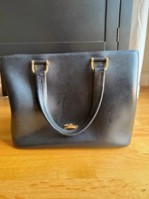 Honore 404 Longchamp - Svart väska från Longchamp. Bra skick, men några fläckar på framsidan, se bild.  Två större öppna fack med ett fack i mitten med dragkedja samt fyra små fack.