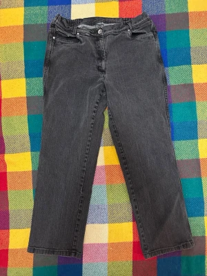 Svarta jeans med broderade bakfickor - Säljer ett par svarta jeans med raka ben och snygga broderade detaljer på bakfickorna. Jeansen har klassisk femficksdesign, knapp och dragkedja fram samt en bekväm midja. Perfekta för dig som gillar enkel stil med en twist.