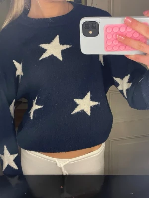 Mörkblå stickad tröja med stjärnor - Säljer en mörkblå stickad tröja med vita stjärnor. Tröjan har en croppad passform och långa ärmar. Så himla snygg! Precis som ny! Storlek 146/152 men passar som xs!