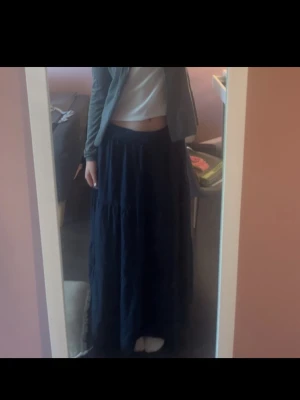 Mörkblå långkjol med resårmidja - Säljer en mörkblå långkjol med bred resår i midjan och flera volanger. Kjolen är luftig och har en flowy känsla, perfekt för dig som gillar en avslappnad men ändå snygg stil. Passar till både sneakers och sandaler.