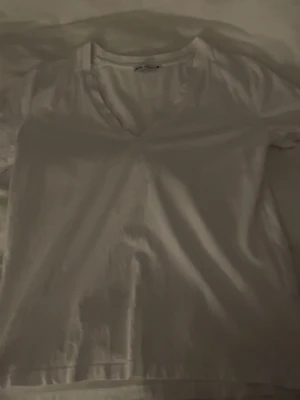 Vit v-ringad t-shirt från Zara - Säljer en enkel och fräsch vit t-shirt från Zara i storlek S. T-shirten har v-ringning och korta ärmar, perfekt för en clean och chill look. Materialet är mjuk bomull som känns skönt mot huden. Passar dig som gillar basic och stilrent.
