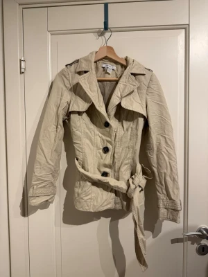 Kort beige trenchcoat  - Jättefin vår/höst jacka med knyte i midjan! Har tyvärr växt ur den:(