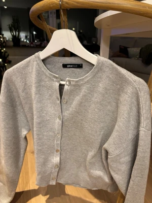 Grå kofta från Gina Tricot - Säljer en stilren grå kofta från Gina Tricot i storlek XS. Koftan har rund hals, långa ärmar och knappar framtill. Materialet är mjukt och stickat, funkar även perfekt för lager-på-lager om man vill ha en blus under🩶