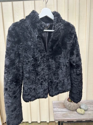 Svart pälsjacka med krage - Mjuk och fluffig svart pälsjacka med klassisk krage och helsvart insida. Jackan har långärmade ärmar och en rak, något croppad passform. Perfekt för dig som vill ha en cool och mysig look under kyliga dagar. Vet inte märket. 