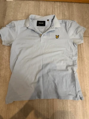 Ljusblå pikétröja från Lyle & Scott - Säljer en ljusblå pikétröja från Lyle & Scott med klassisk krage och korta ärmar. Är skrynklig, men bara att Stryka en gång.