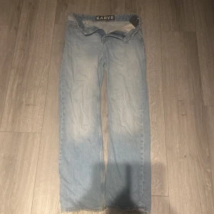 Ljusa jeans från Karve med rå kant - Säljer ett par ljusblå jeans från Karve med rak passform och sliten kant längst ner. Klassisk femficksmodell med bälteshällor och knappstängning. Jeansen har en avslappnad vibe och är tillverkade i jeansmaterial.