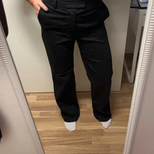 Svarta kostymbyxor med rak passform - Snygga svarta kostymbyxor med rak och lite loose passform. Byxorna har bälteshällor, dold dragkedja och knapp framtill. Materialet känns mjukt och har en klassisk look som funkar till många olika stilar. Perfekta om du gillar en clean och enkel vibe.