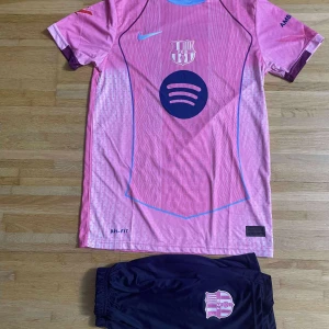 Barça Raphinha rosa matchtröja Nike - Säljer en FC Barcelona matchtröja med Raphinha #11, i rosa med lila detaljer och tryck. Tröjan har korta ärmar, Dri-Fit material och klubbmärke samt sponsorloggor. Ingår även mörkblå shorts med rosa Barça-emblem. Perfekt för dig som älskar fotboll och Barça.