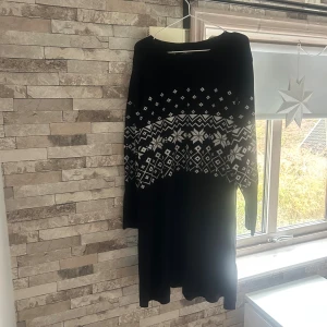 Svart stickad långklänning bpc  - Svart stickad långklänning från bpc bonprix collection i storlek 2XL. Klänningen har ett snyggt vitt mönster över bröstet och axlarna, långa ärmar och rund halsringning. Perfekt för kalla dagar när du vill vara både bekväm och stilren.