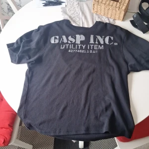 Svart GASP t-shirt med tryck - Cool svart t-shirt från GASP med stort, slitet tryck på både fram- och baksidan. Modellen är kortärmad och tillverkad i ett mjukt bomullsmaterial. Perfekt för dig som gillar sportig och avslappnad stil.