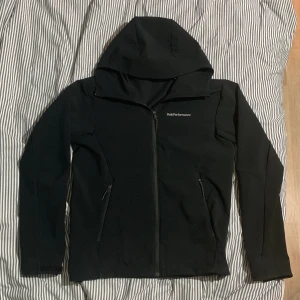 Svart vindjacka Peak Performance  - Svart vindjacka från Peak Performance i storlek S. Jackan har huva, hel dragkedja framtill och två sidofickor med dragkedja. Diskret logga på bröstet och ärmen. Perfekt för dig som gillar stilren och funktionell design. Den är både vattentät och vindtät. Det finns inga slitningar på jackan.