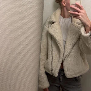 Beige teddyjacka med dragkedja - Säljer en beige teddyjacka med bred krage och coola dragkedjedetaljer. Jackan är fluffig och har en oversized passform som ger en chill vibe. Perfekt att slänga på över en t-shirt för en avslappnad look.