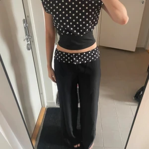 Svarta wide byxor med prickig midja - Snygga svarta byxor med breda ben och en unik midja i svart tyg med vita prickar. Byxorna har en loose passform och sitter lågt på höften. Perfekt för dig som gillar statement-plagg och vill sticka ut med coola detaljer.