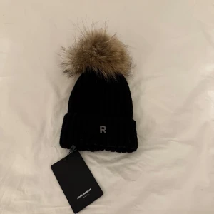 Mössa med pälsboll - Mössa från Rockandblue med äkta päls. Köpte den förra året för 499kr. Den är helt oanvänd med lapparna kvar. 