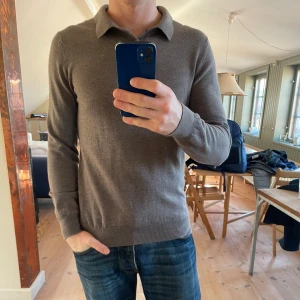 Brun pikétröja i ull från John Henric - Snygg brun pikétröja från John Henric i mjuk ull. Tröjan har klassisk krage, två knappar vid halsen och långa ärmar. Passformen är normal och materialet känns lyxigt och skönt mot huden. Perfekt för dig som gillar stilrena och tidlösa plagg. Skick 10/10. Storlek L men sitter M. Hör av dig vid frågor eller om bilder behövs.MVH/Bpluggen