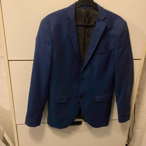 Blå kostym Jack & Jones super slim - Snygg marin blå kostym från Jack & Jones i super slim passform och är använd 1-2 gånger, säljs på grund av att den är för liten för mig. Nypris ligger på 1-2000. Kavajen har klassisk krage, två framfickor med lock och en bröstficka. Byxorna är raka med pressveck och bälteshällor. Materialet är mjukt och lätt, perfekt för dig som gillar stilren look.