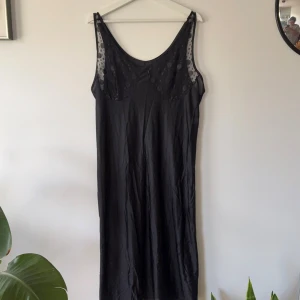 Svart långklänning med meshdetaljer - Svart långklänning med ärmlös design och meshpartier upptill med prickigt mönster. Klänningen har en rak och enkel siluett, djup rundad halsringning och transparenta detaljer vid axlarna. Perfekt för dig som gillar stilrena och coola plagg.