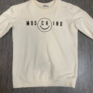 Vit sweatshirt - Vit sweatshirt med svart tryck och smiley på bröstet. Köpt här på plick men var för liten. Kan inte garantera äkthet där av priset & finns en liten fläck vid nacken på baksidan av tröjan, har inte testat att tvätta den vill bara bli av med den, använd få gånger. Skriv vid funderingar!