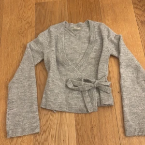 Mysig grå kofta - Mysig grå stickad kofta från Gina Tricot i storlek XS. Koftan har långa ärmar, knytband i midjan och en djup v-ringning. Säljer pga ingen användning 