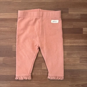 Rosa leggings - Supersöta rosa leggings med borstad insida från Newbie i storlek 62 (2-4mån). Fina volangdetaljer längst ner vid bensluten. Använt fåtal gånger och i mycket fint skick. Lite blekt bak vid taggen.