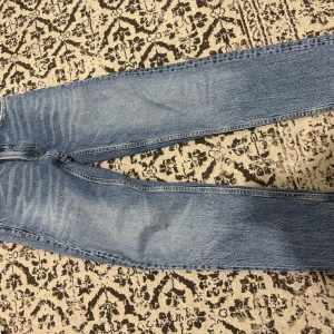 Levi's 501 ljusblå jeans straight fit - Säljer ett par klassiska Levi's 501 jeans i ljusblå tvätt med raka ben och fem fickor. Jeansen har en ikonisk knappgylf och subtila slitningar som ger en cool vintagekänsla. Perfekt för dig som gillar tidlös stil och vill ha ett par jeans som funkar till allt.