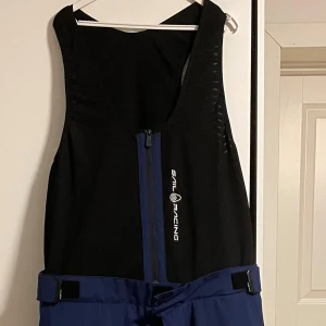 Sail Racing Gore-Tex täckbyxor blå/vit - Säljer ett par helt nya aldrig använda (med etiketter) Sail Racing täckbyxor med hängslen i blått, vitt och grått. Byxorna har dragkedja framtill, justerbara band i midjan och flera fickor med vattentäta dragkedjor. Tillverkade i Gore-Tex material som håller dig torr och skyddad under tuffa väderförhållanden. Pris kan diskuteras vid snabb affär.